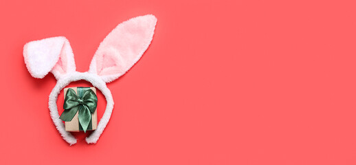 Bunny ears and Christmas gift on red background with space for text
