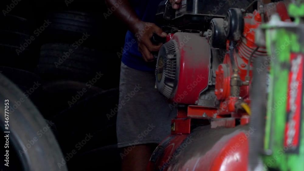 Poster slow motion - a man starting air compressor belt driven machine manually on workshop