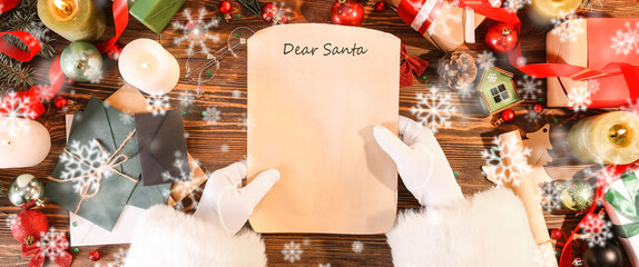 Hands of Santa Claus with letter on wooden background with Christmas decor, top view
