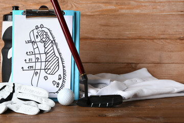 Clipboard with drawn scheme of golf game, bottle, club, ball, glove and clothes on wooden background