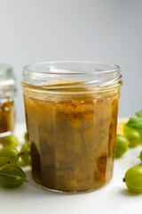 Jar of delicious gooseberry jam and fresh berries on white table, closeup