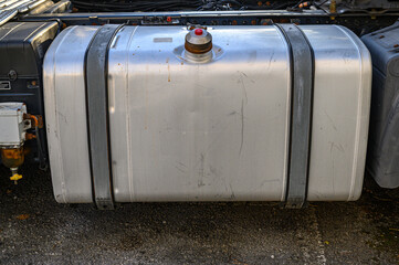 close-up of a silver aluminum fuel tank, attached by two braces to the outside of a tractor unit, truck