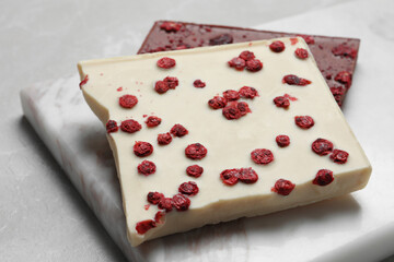 Board and different chocolate bars with freeze dried fruits on light marble table, closeup