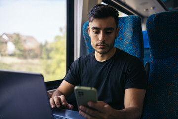 Young man working with laptop and smartphone in the train