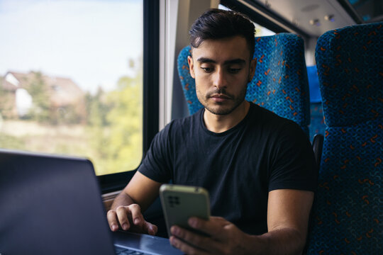 Young man working with laptop and smartphone in the train
