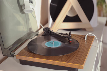 Stylish turntable with vinyl disc and headphones on white chest of drawers at home