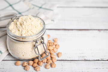 Glass jar with chickpea flour and seeds on white wooden table, space for text