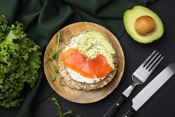 Crunchy buckwheat cakes served with cream cheese, salmon and avocado on black table, flat lay
