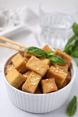 Bowl with delicious fried tofu, basil and sesame seeds on white table