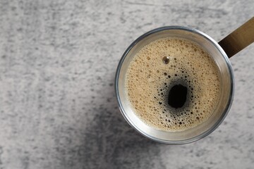 Turkish coffee pot with hot drink on grey table, top view. Space for text