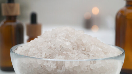Glass bowl with bath salt and cosmetic products indoors, closeup
