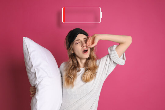 Tired woman with sleeping mask, pillow yawning and illustration of discharged battery on pink background