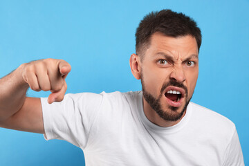 Aggressive man pointing on light blue background