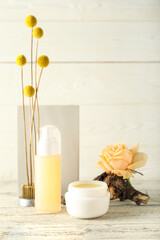 Cosmetic bottle with jar of cream, decor and ikebana on white wooden background