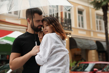 Young couple with umbrella enjoying time together under rain on city street