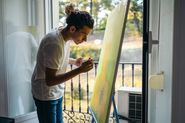 Young artist painting a canvas near a balcony