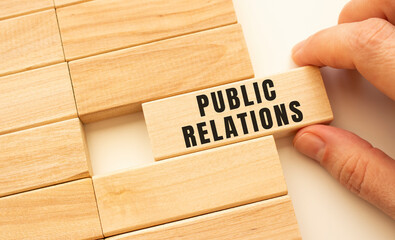Hand holds a wooden cube with the text PUBLIC RELATIONS.