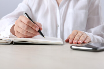 Fototapeta premium Woman writing in notebook at wooden table in office, closeup