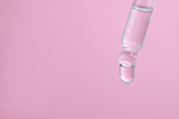Dripping serum from pipette on pink background, closeup. Space for text
