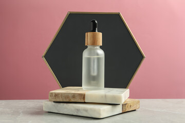 Bottle of face serum with marble boards on grey table against pink background