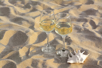 Glasses of tasty wine and seashell on sand, space for text