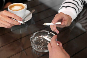 Women holding cigarette over glass ashtray at table, closeup