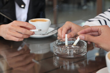 Fototapeta na wymiar Women putting out cigarettes in ashtray at table, closeup