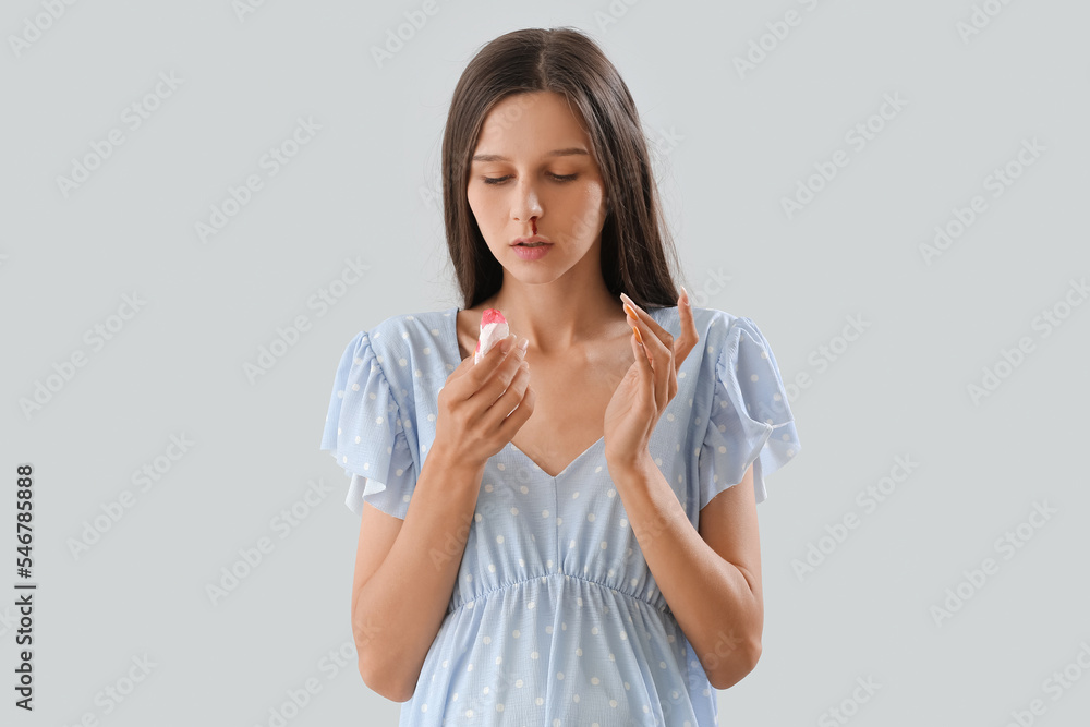 Wall mural Young pregnant woman with nosebleed and tissue on light background