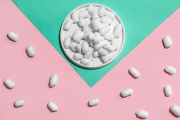 Plate of soft cotton balls on color background