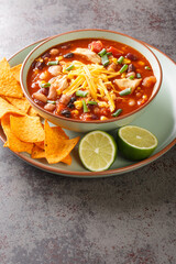 Hearty chicken taco soup packed with black beans, corn, and tomatoes with green chile peppers close-up in a plate on the table. Vertical