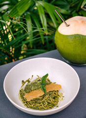 Spaghetti with pesto and coconut under palm tree