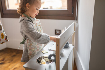 little girl playing cooking with her toy kitchen at home