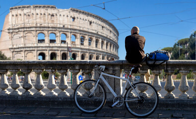 man sitting on low wall looks at the sea with bike in Rome with Colosseo