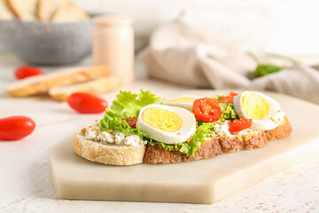 Board of tasty toast with boiled egg and tomatoes on light background, closeup
