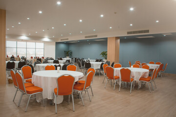 Round table with a white tablecloth, orange and black chairs in a modern restaurant or banquet room...