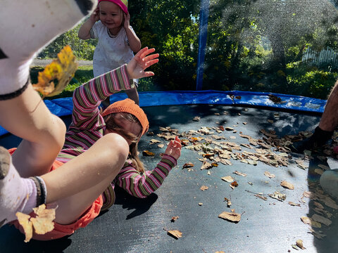 Small girls wearing warm hats are jumping and falling on a tramp