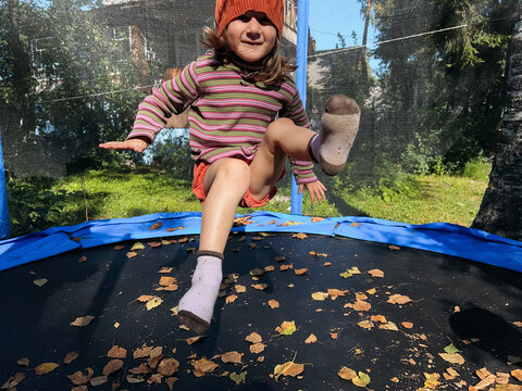 Small girl wearing a beanie hat is tumbling on a trampoline 