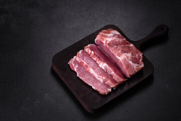 Fresh piece of raw pork with spices, salt and herbs on a wooden cutting board
