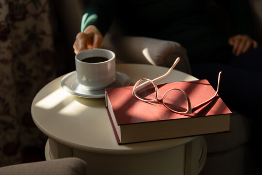 Detail shot - hand putting coffee mug on table with book and glasses