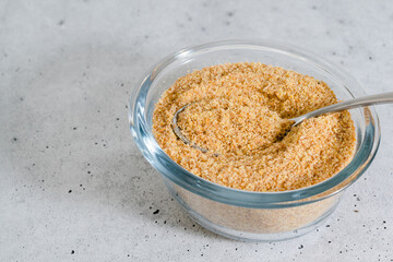 Flaxseed meal close up in a glass bowl on light grey stone background