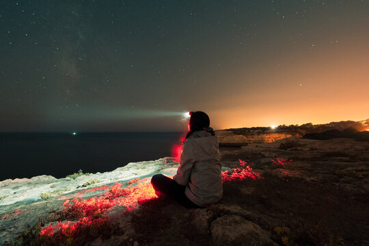 Sitting woman with head flashlight during starry night