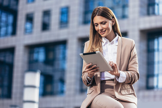 Attractive businesswoman using a digital tablet while sitting in front of business building.