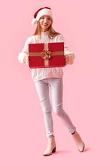 Young woman in Santa hat with Christmas present on pink background