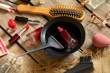 Brushes and lipstick, combs and shadows, perfumes and various cosmetics lie on a wooden background,...