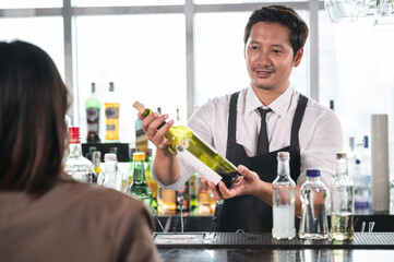 Asia bartender show wine bottle to customer at the bar counter with city background at hotel	