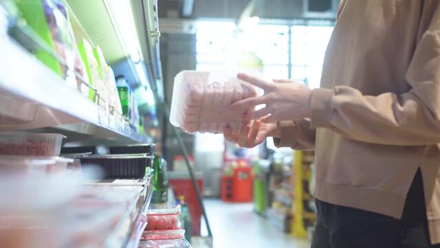 picks out minced meat in the supermarket's refrigerated compartment.
