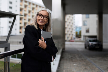 gray-haired businesswoman with a laptop in her hands against the backdrop of an office building