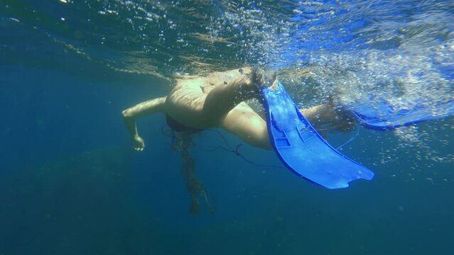 POV following a female free diver with blue flippers going to the bottom of the ocean with coral reefs. Girl exploring wild nature in warm sea near old rope. Film grain pixel texture. Swimmer