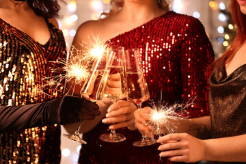 Obraz na płótnie Canvas Young women holding glasses of champagne and Christmas sparklers, closeup