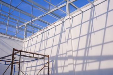 Aluminum c-line ceiling structure and scaffolding with white concrete wall in house construction site against blue sky background, low angle and perspective view